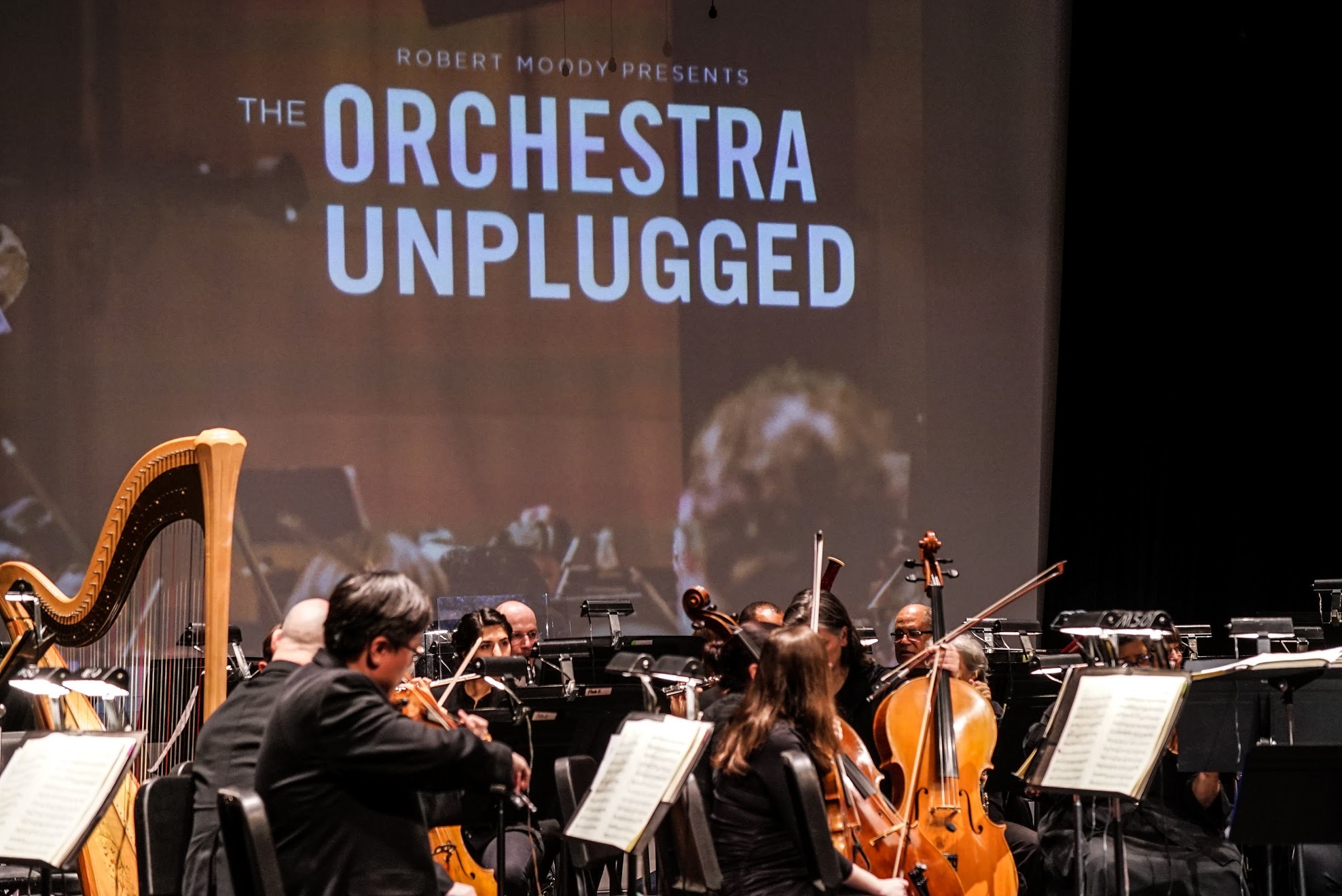 Orchestra playing with Orchestra Unplugged Logo projected onto screen.